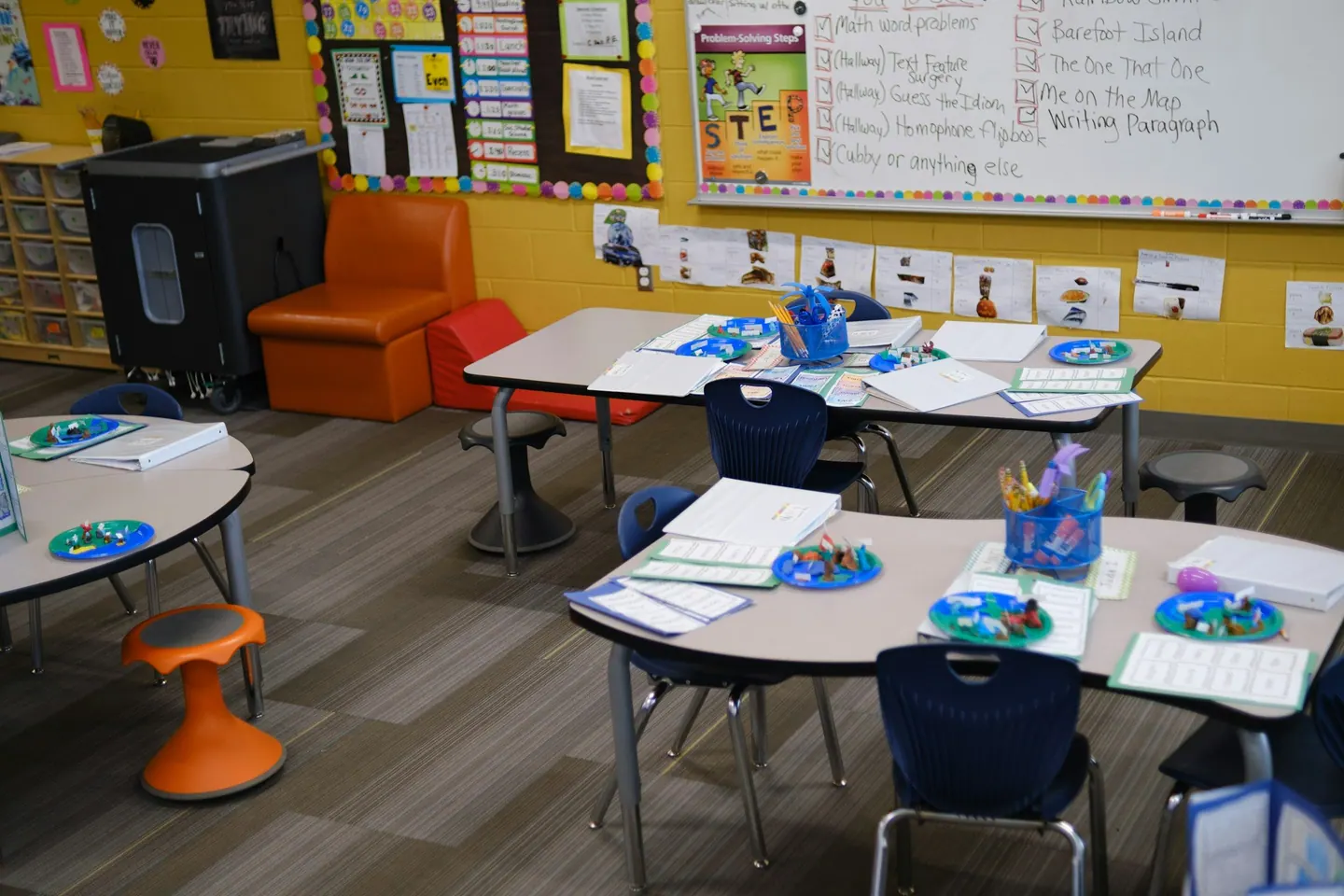 Aula de primaria con mesas de grupo, sillas azules, material escolar y murales de colores